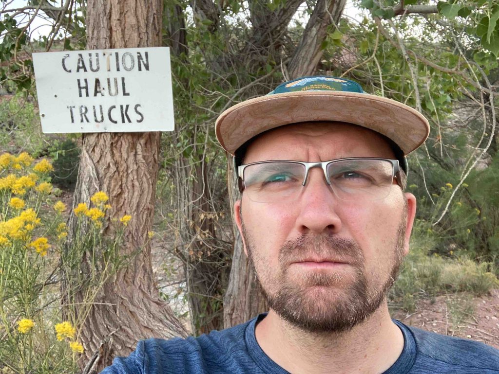 Picture of Daniel Barney out hiking on a haul truck road. A sign in the background reads: "CAUTION HAUL TRUCKS"